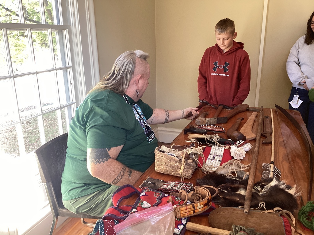 A man shows traditional tools and artifacts to a student inside a historic building.