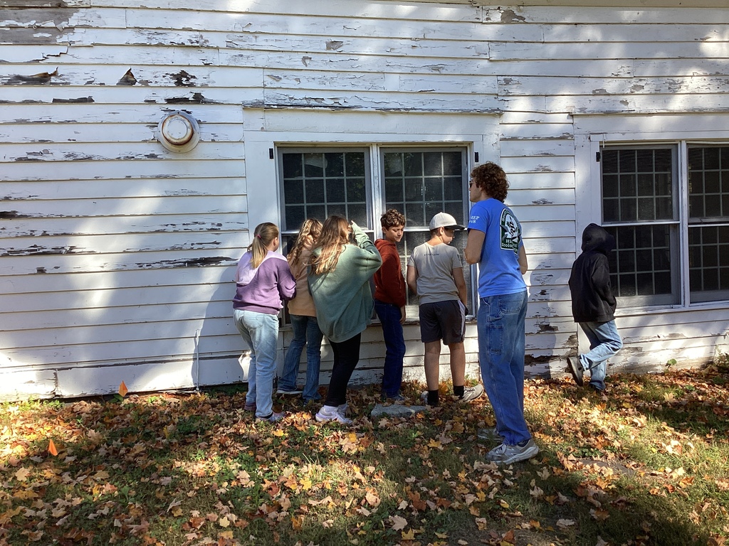Students examine the outside of a historic white clapboard building.