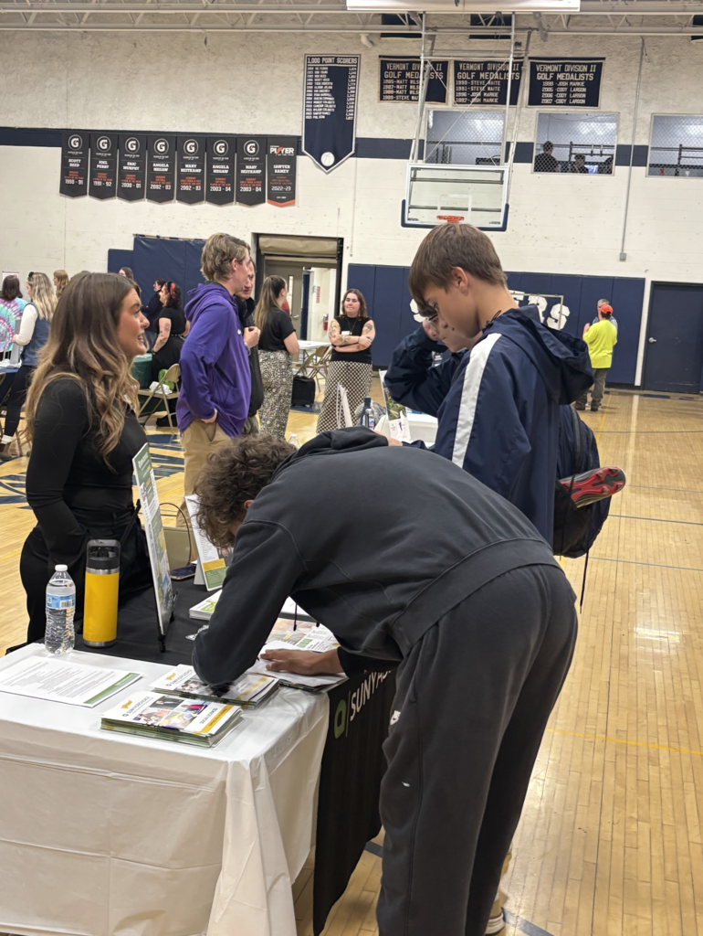 Students visit a booth at a career fair in a gymnasium, speaking with a representative and filling out forms.