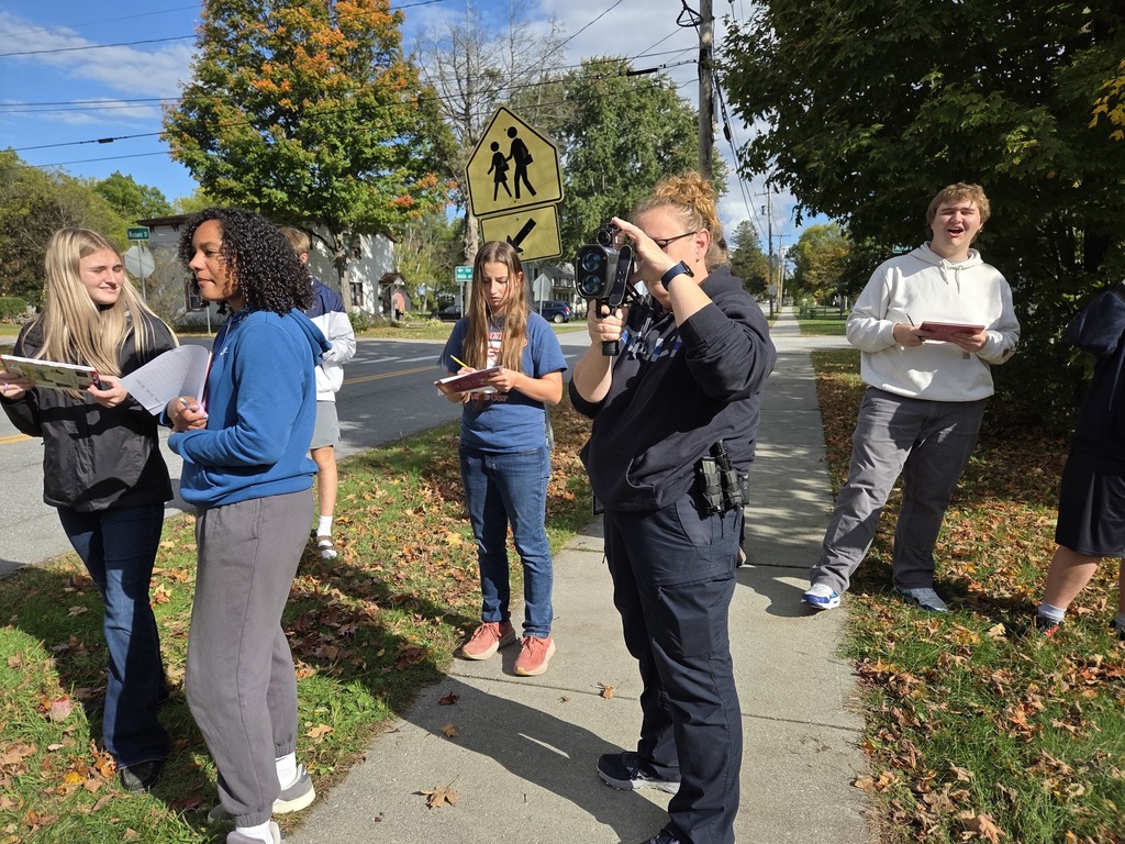 A group of students and a school resource officer use a radar device and take notes during an outdoor lesson.