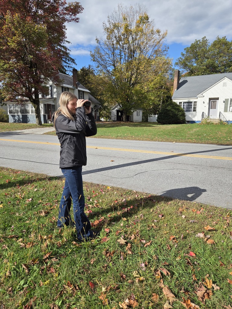 A student uses a radar gun while another student looks through binoculars across the street.