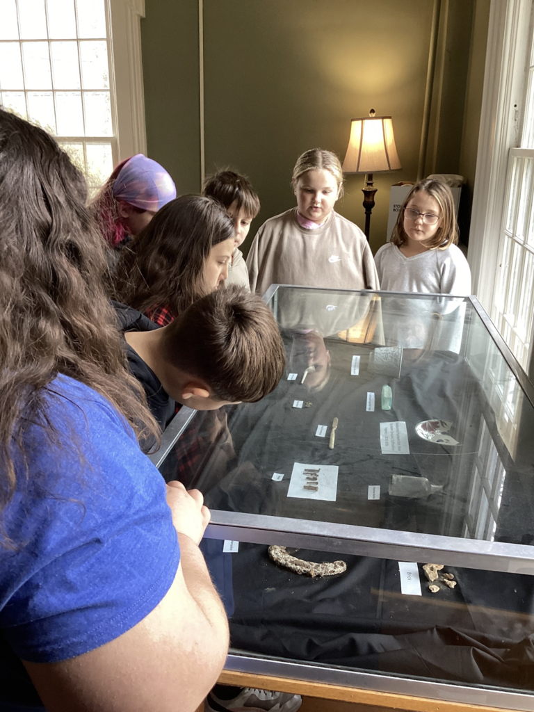 A group of students view historical artifacts displayed in a glass case inside a museum-like room.