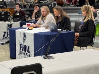 Three presenters sit at a table with microphones and laptops at a meeting marked with FHU Slaters logos.
