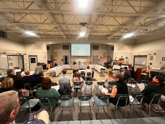 Attendees sit in rows facing a presentation area during a Vermont State of Education school board meeting.