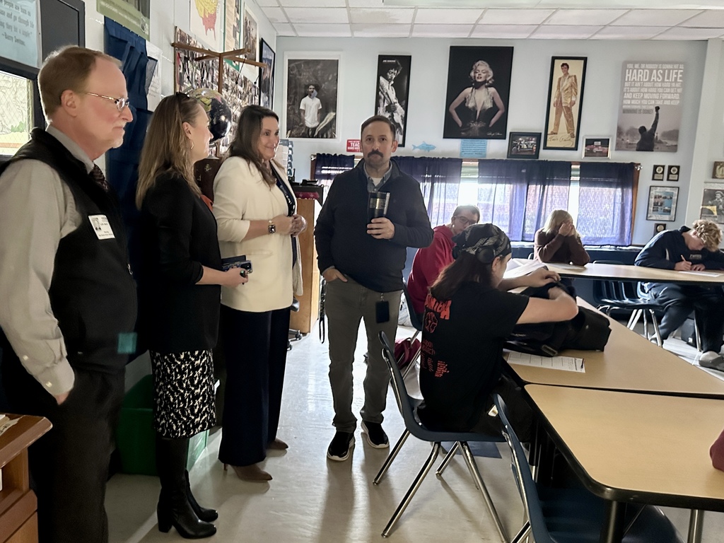 School administrators and visitors stand at the front of a classroom speaking with students during a visit.