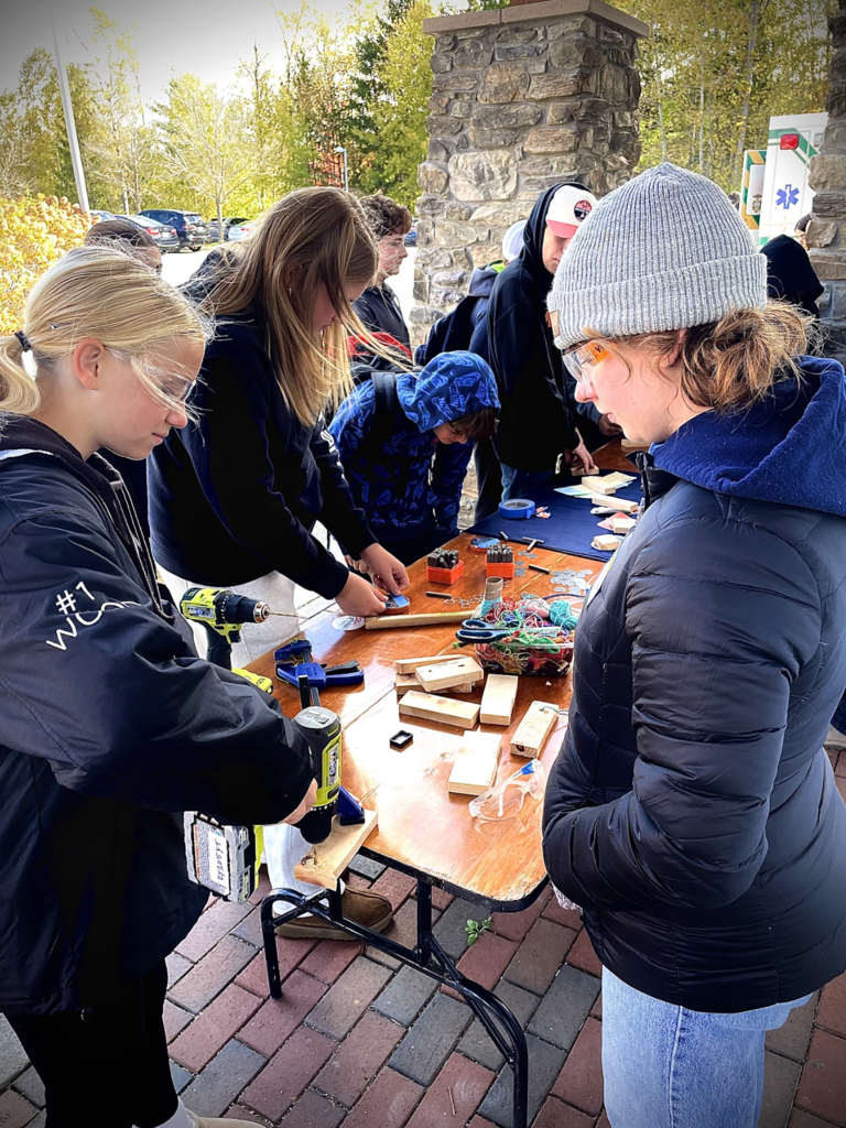 Students use drills and clamps on wooden projects during an outdoor workshop.