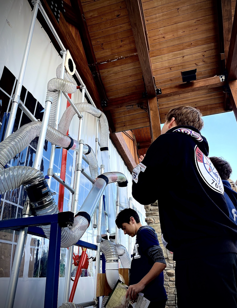 Students interact with a wall display of clear tubing and airflow mechanisms.