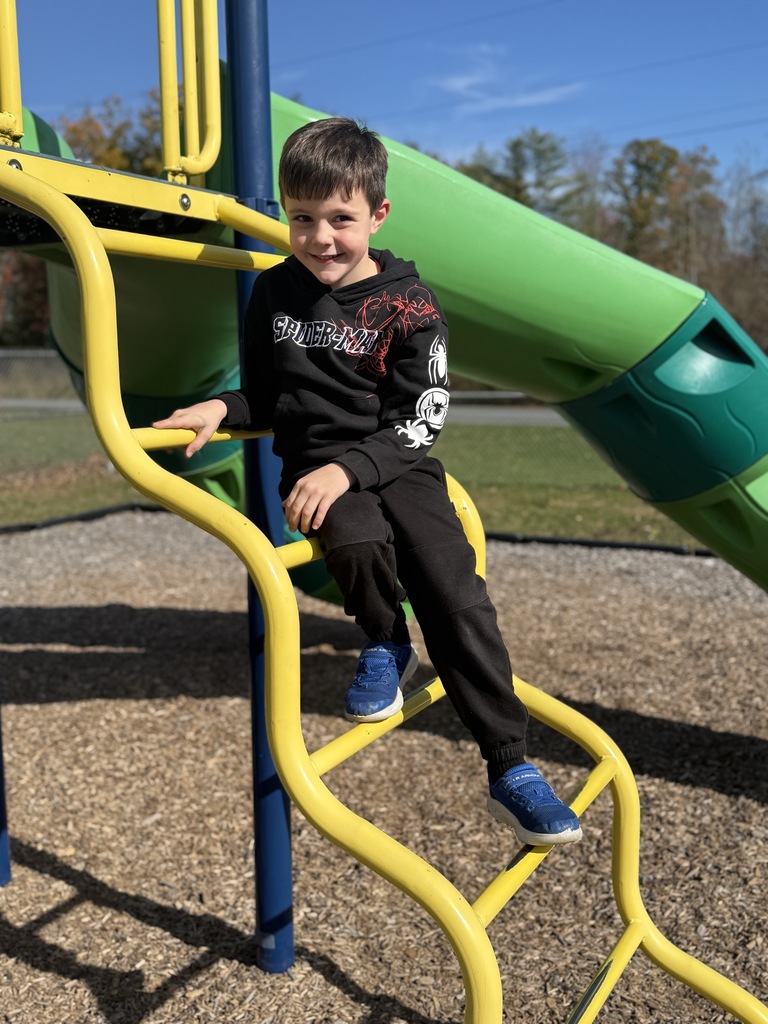 A boy in a black outfit sits on a yellow playground ladder, smiling at the camera.