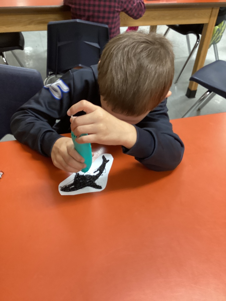 Student concentrating while using a turquoise 3D pen to design an orca whale.