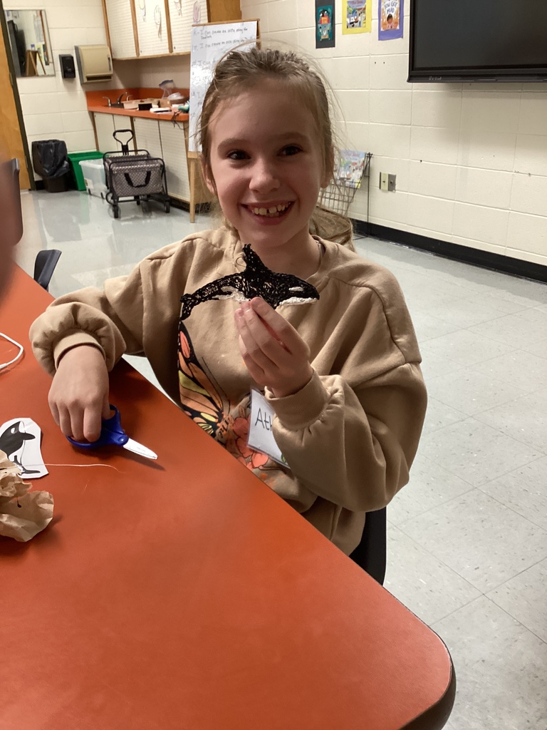 Smiling student holding up a completed black orca whale 3D creation.