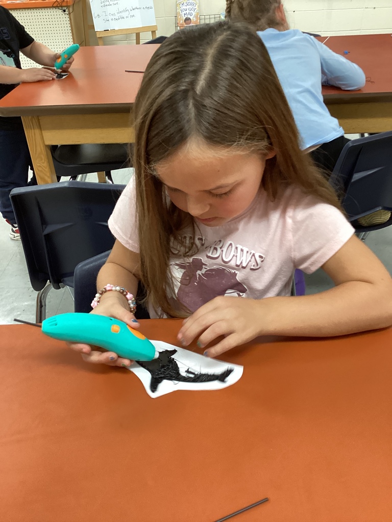 Student working carefully with a 3D pen to create a black orca whale design.