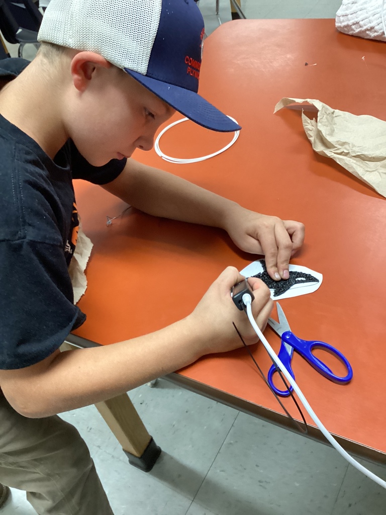 Student wearing a cap using a black 3D pen to trace an orca whale template.