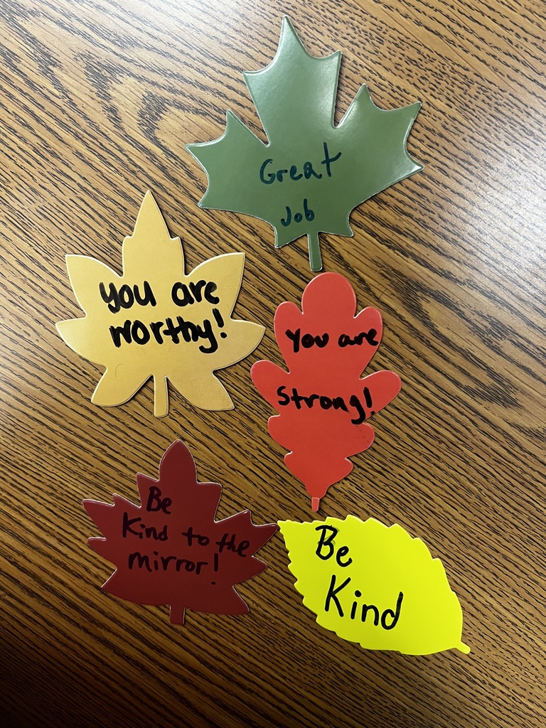 Five colorful paper leaves on a table with handwritten affirmations such as “You are worthy!” “Be kind,” and “Great job.”