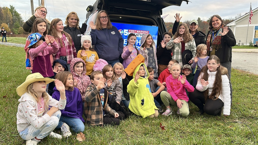 Group of smiling Benson Village School students and staff wave while posing in front of the NBC 5 weather lab van during the morning broadcast.