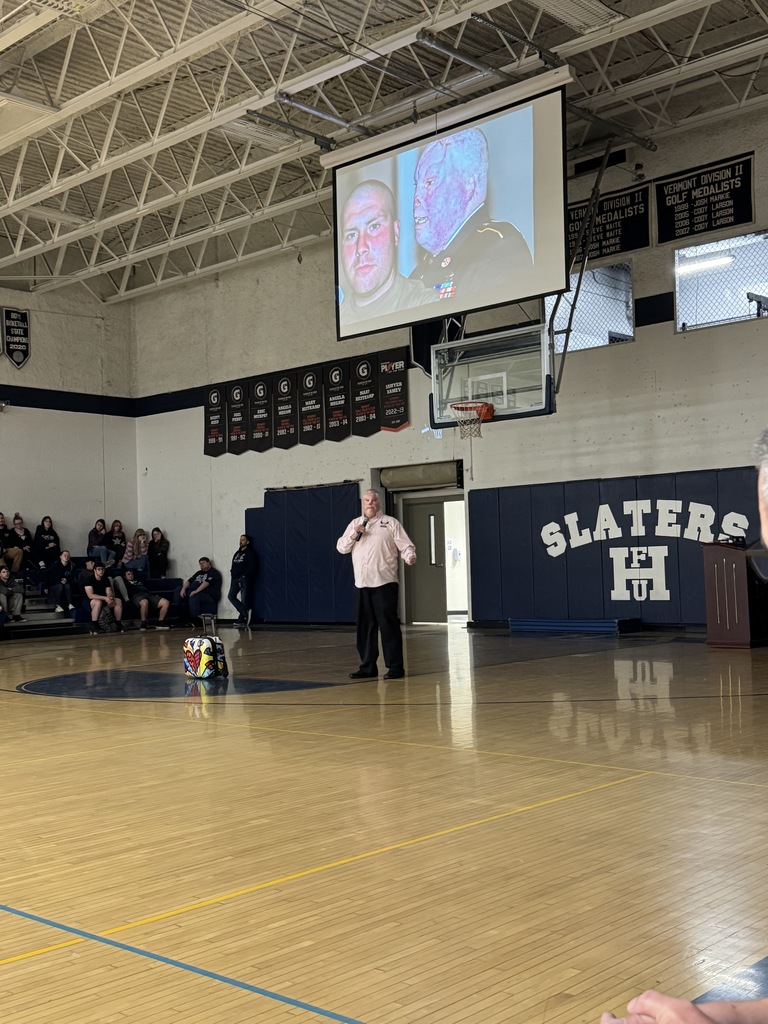 A presenter speaks in front of a large projected image showing before-and-after photos of a man’s recovery from burn injuries. Students sit in the bleachers, watching attentively.