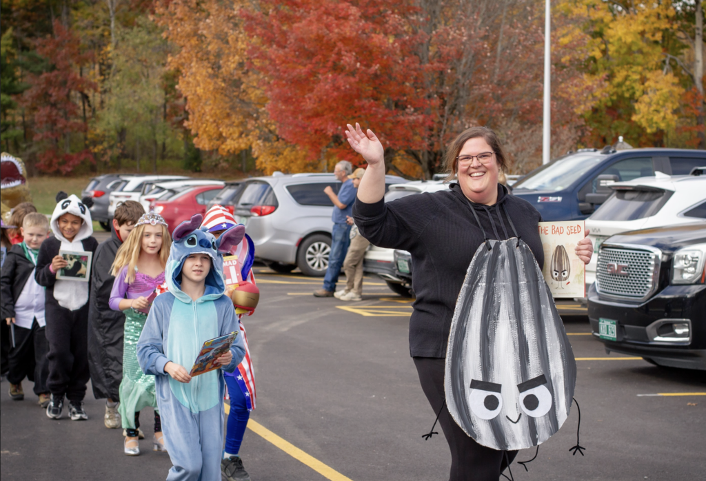 A teacher dressed as a "Bad Seed" and carrying the book leads her students who are dressed in various book character costumes, including Disney's Stitch, a Mermaid, Captain America and a Panda Bear.