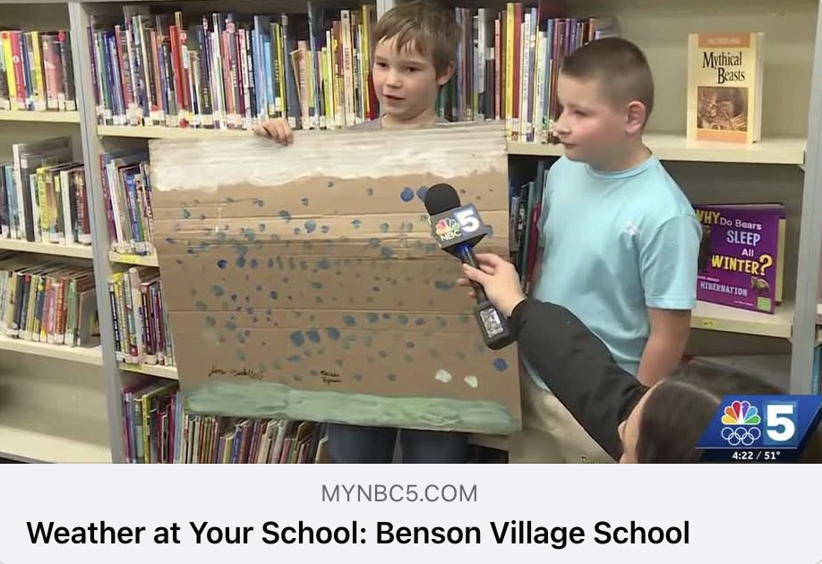 screenshot from NBC5's Weather at Your School at Benson Village School, showing students holding a weather map of rain, they are talking into a newscaster's microphone