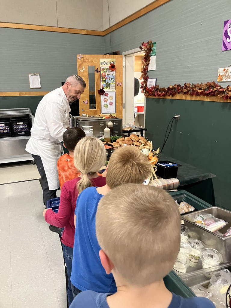 A chef serves sandwiches to a line of young students in the cafeteria.