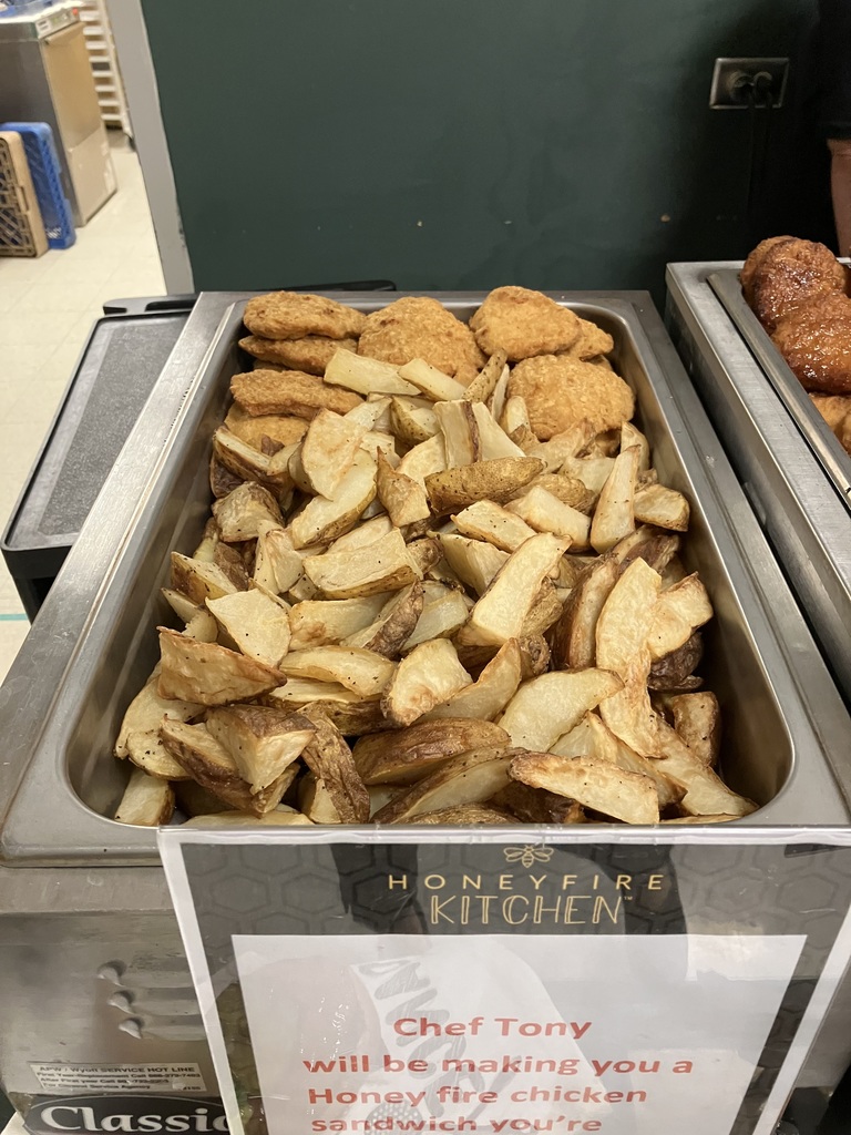 A tray of roasted potato wedges and crispy chicken patties labeled “Honeyfire Kitchen” at the cafeteria serving station.