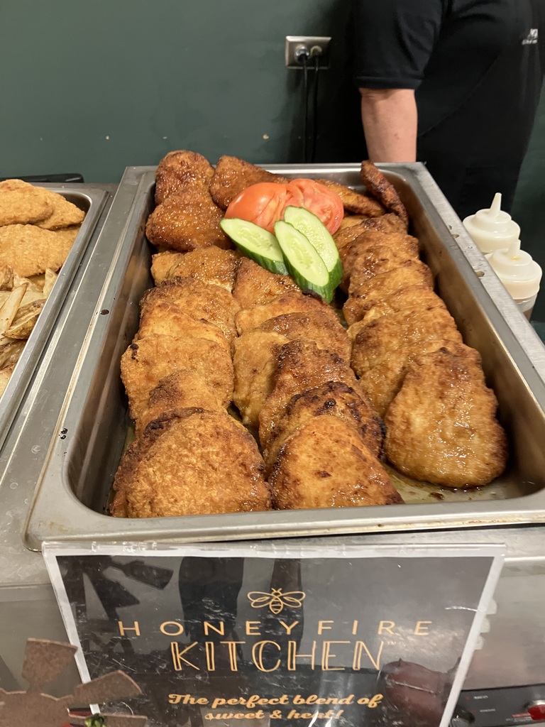 A close-up of Honeyfire Kitchen’s tray of golden brown chicken pieces garnished with sliced tomatoes and cucumbers.