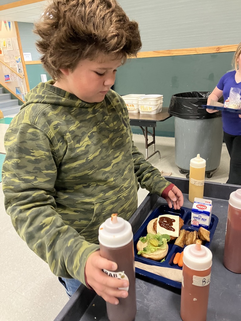 A student in a camouflage hoodie adds sauce to a sandwich at the condiment station.