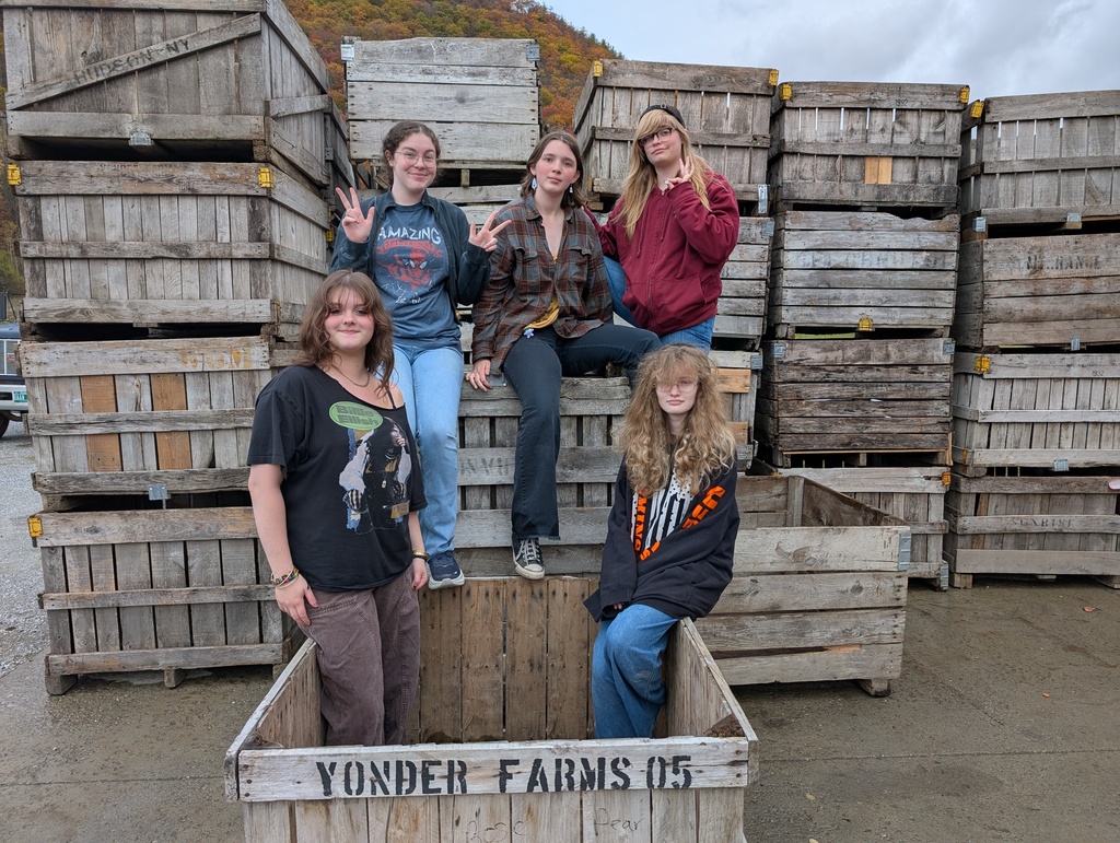 Five Annex students pose and smile while standing and sitting among large wooden farm crates labeled “Yonder Farms,” with colorful autumn foliage visible in the background.