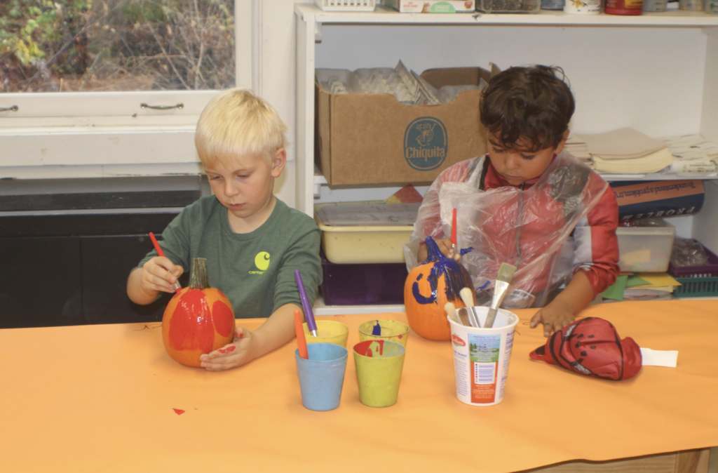 Two students carefully paint pumpkins red and blue while seated at a craft table.