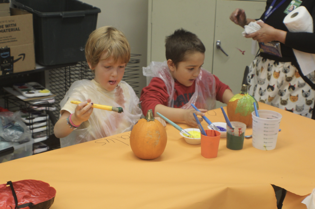 Two children focused on painting pumpkins green and yellow during Book Character Day.