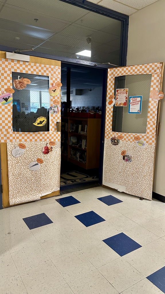 Double library doors decorated with orange checkered and polka-dot paper, pumpkins, and fall-themed cutouts.