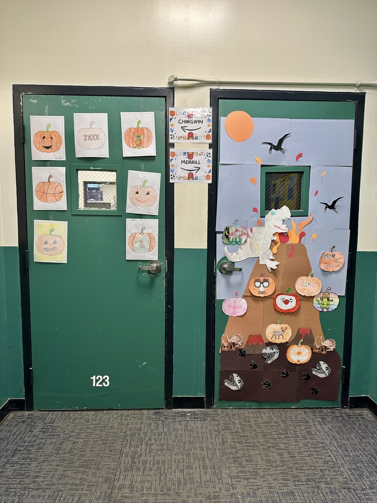 Two green classroom doors decorated with pumpkins and dinosaurs; one door features a volcano and flying pterodactyls.