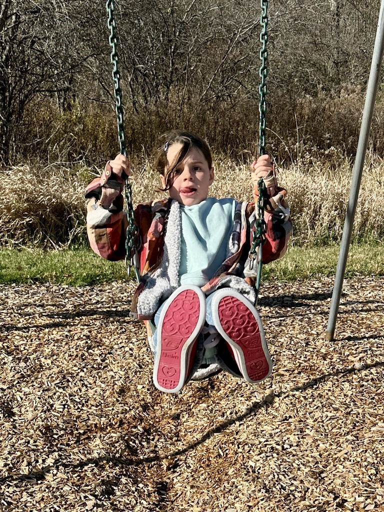 Girl swings on a playground swing on a sunny day, looking toward the camera.