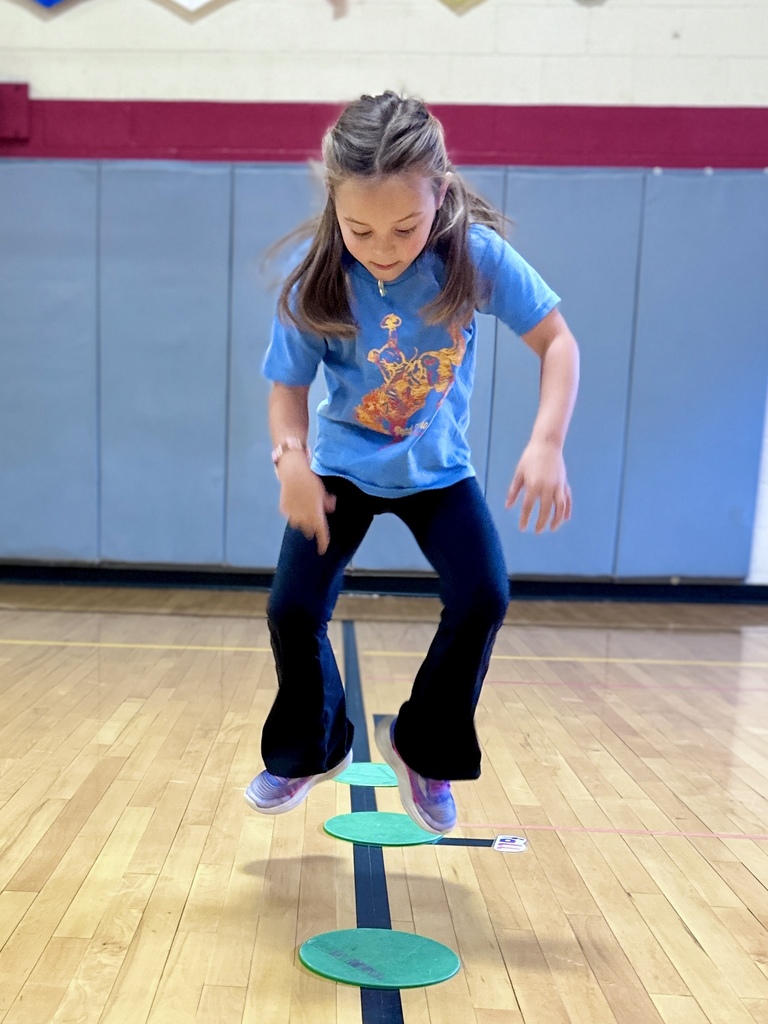 Girl jumps between circular floor markers during an activity in the school gym.