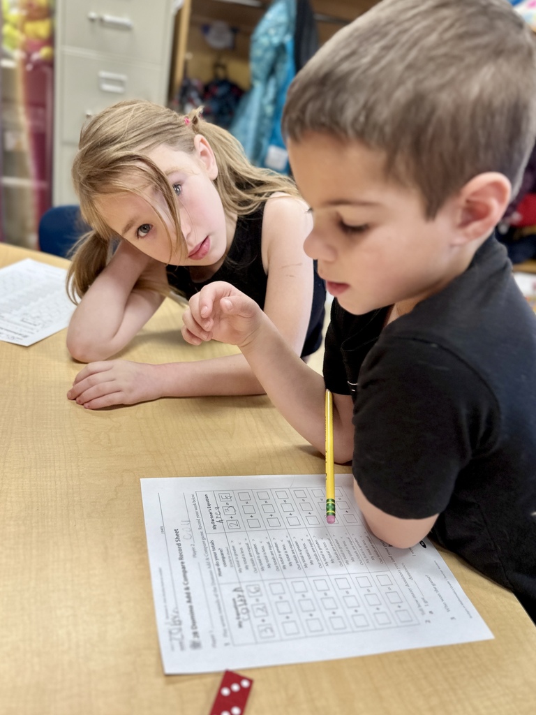 Two students work together at a desk on a math worksheet, using a pencil and counting dice.
