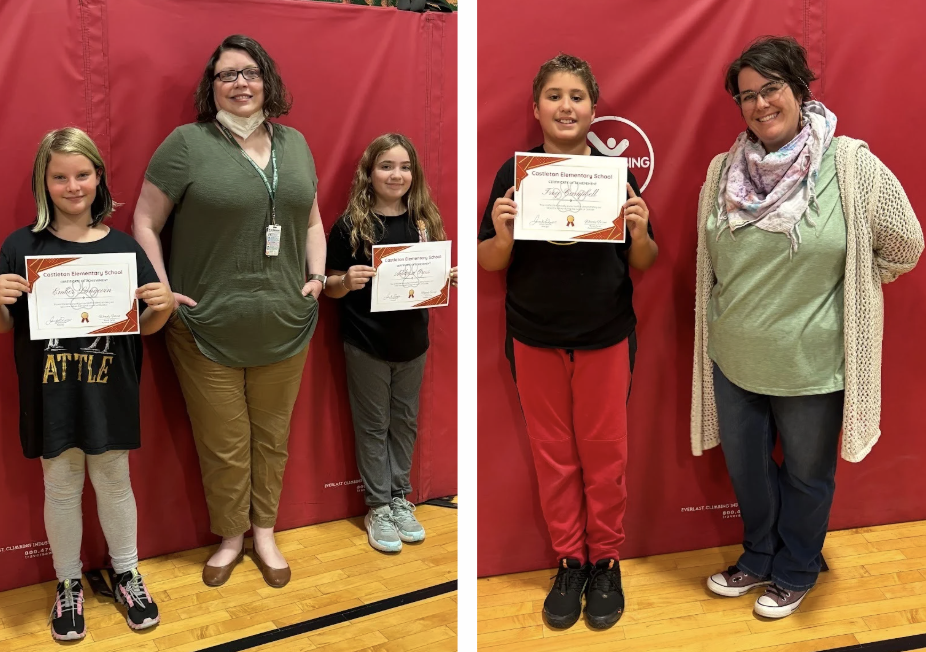 Two students standing with an adult in front of a red gym mat; both students hold certificates and Student holding a certificate stands next to an adult in front of a red gym mat.