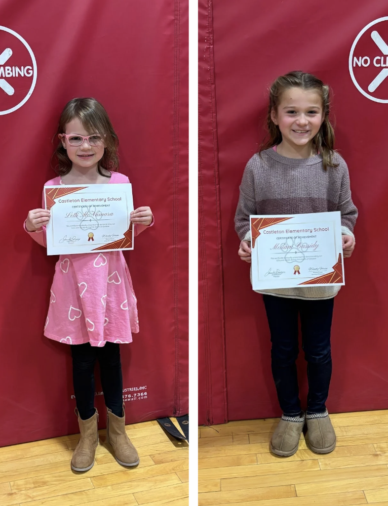 Young students standing in front of a red gym mat holding a certificate and smiling.