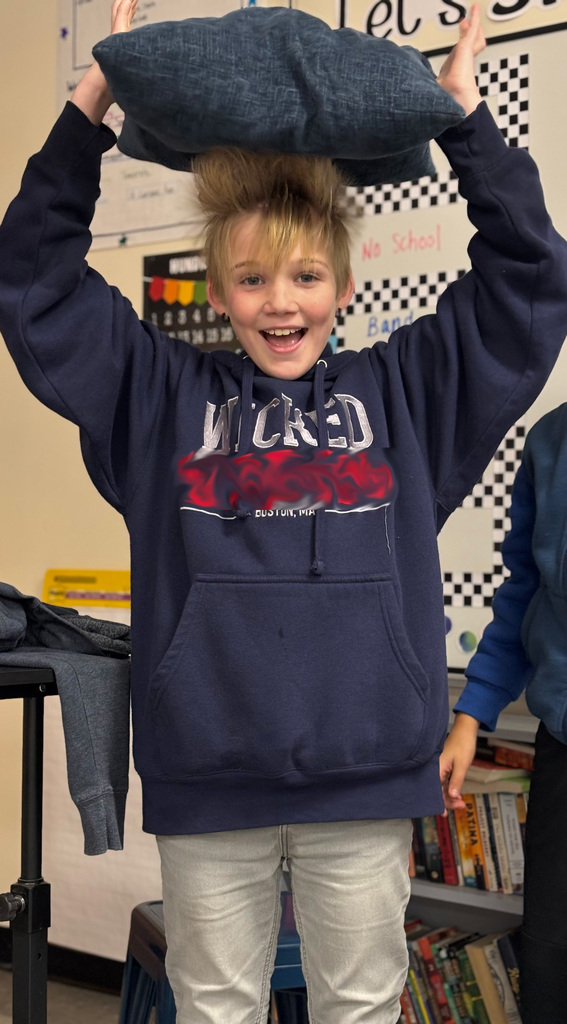 A smiling student holds a pillow over their head as their hair stands straight up from static electricity.
