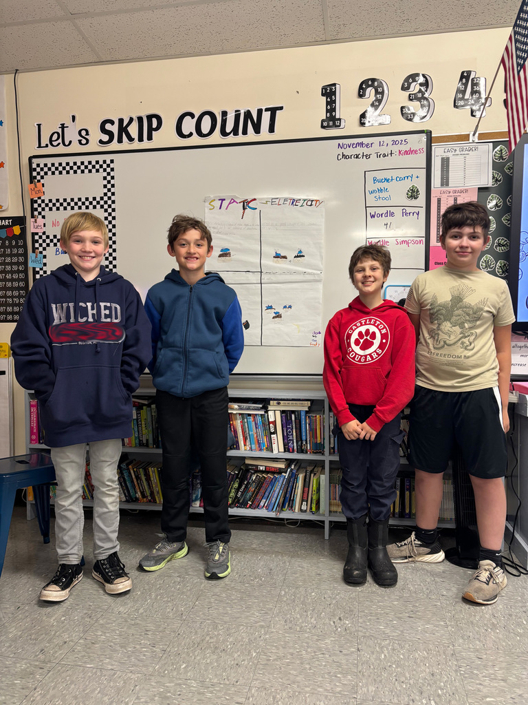 Four boys stand in front of a whiteboard displaying their “Static Electricity” project poster, smiling for the camera.