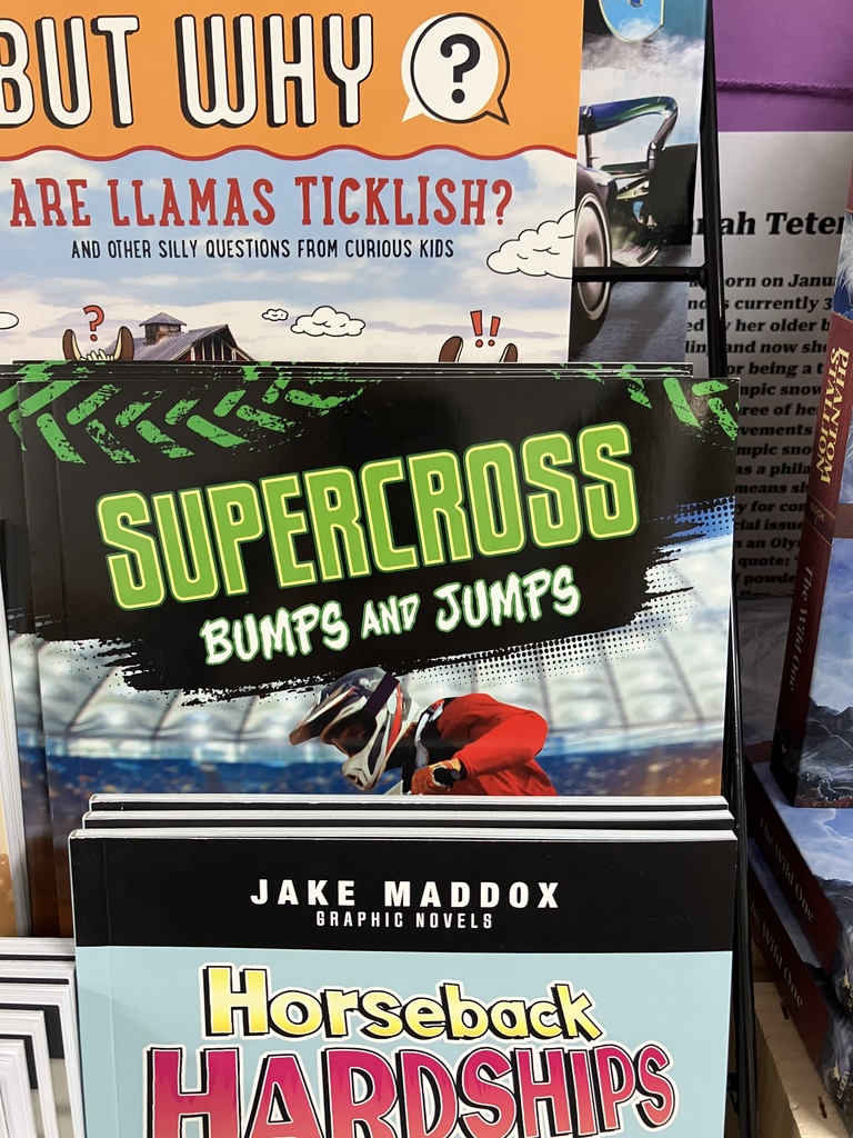 A close-up shot of two book covers: the top book is a question-based title asking, "BUT WHY ARE LLAMAS TICKLISH?" The bottom book cover is a sports title titled "SUPERCROSS BUMPS AND JUMPS." Classroom Photos
