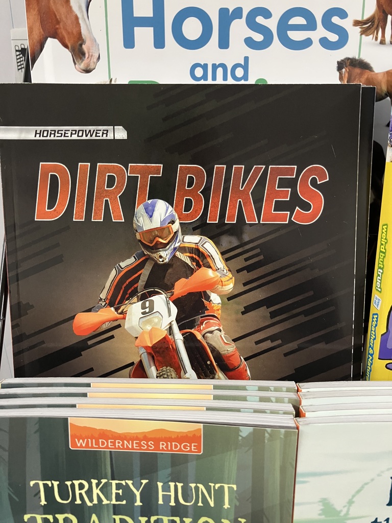 A close-up shot of the cover of a non-fiction children's book titled "DIRT BIKES" in large, red and white letters. The cover features an image of a person riding a dirt bike in racing gear.