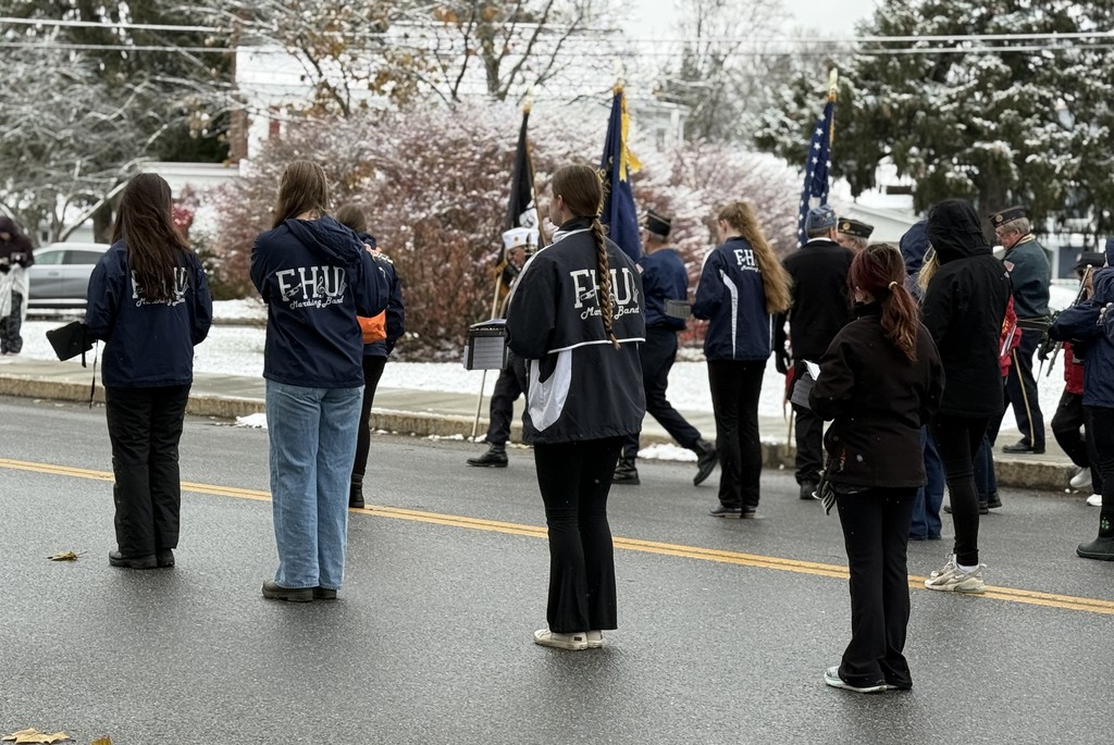 FHU marching band members stand on the road with instruments as the veterans’ color guard walks ahead of them.
