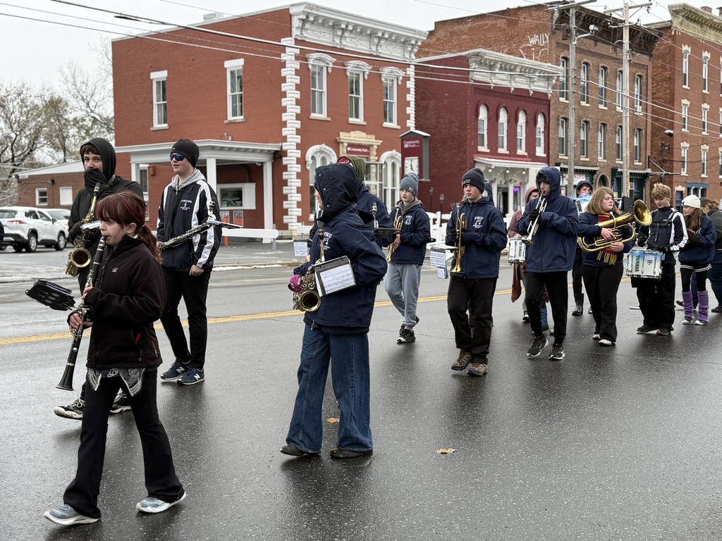FHU marching band students play brass, woodwind, and percussion instruments as they march down the street.