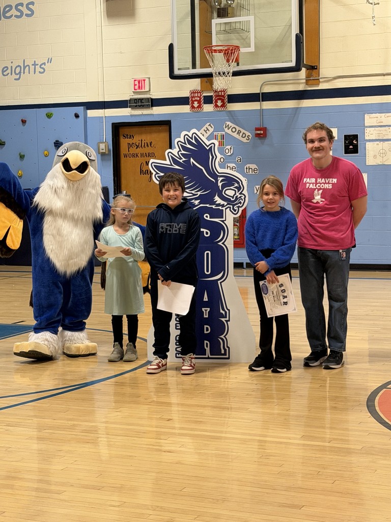 One adult, three children holding certificates, and a school mascot stand together in a gymnasium for a photo.