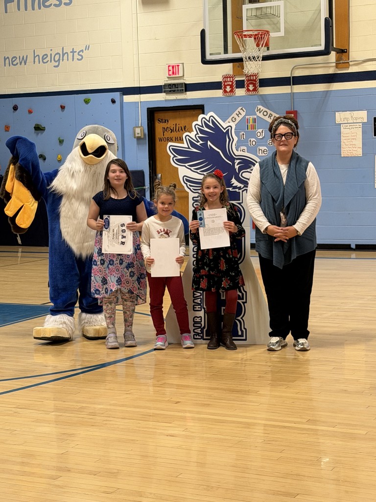 One adult, three children holding certificates, and a school mascot stand together in a gymnasium for a photo.