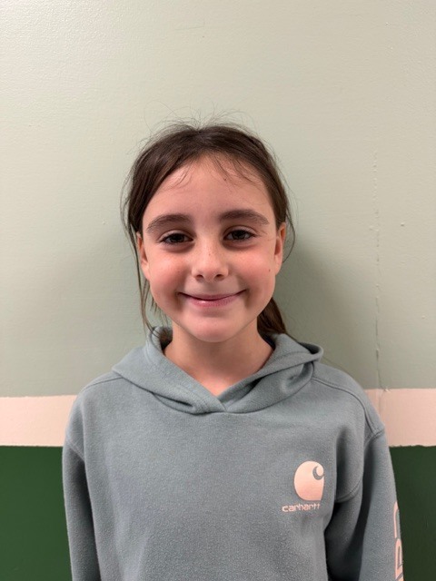 A girl with brown hair pulled back in a ponytail smiles while wearing a light blue Carhartt hoodie.