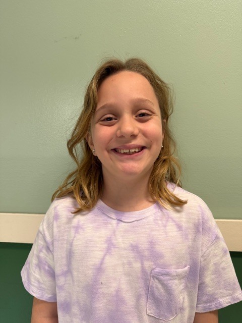 A girl with shoulder-length blonde hair smiles while wearing a lavender tie-dye T-shirt.