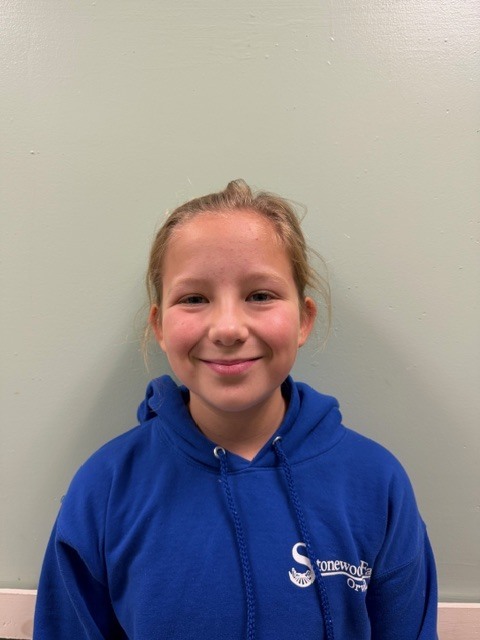 A girl with blonde hair smiles at the camera while wearing a royal blue hoodie.