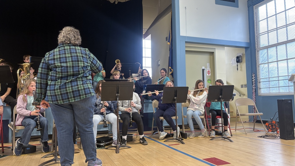 5th–6th grade band students play woodwinds and brass as the director conducts from the front of the stage.
