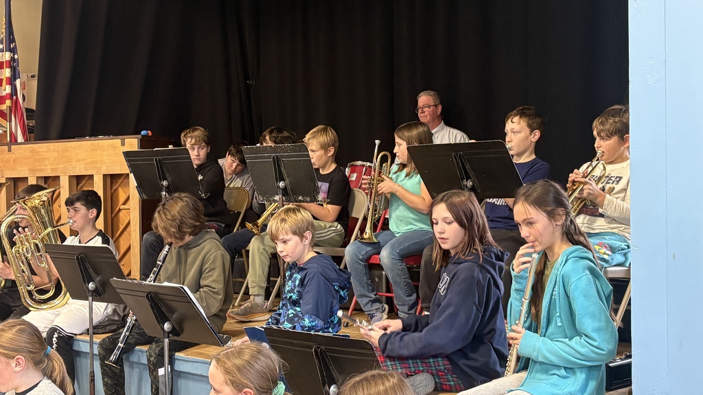 The full 5th–6th grade band performs onstage, playing brass and woodwind instruments, with Principal Walters on drums in the back row.
