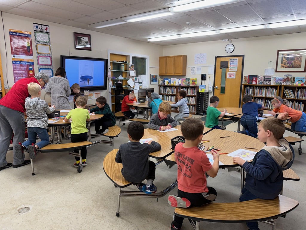A classroom of kindergarteners work at tables on coloring and assembling owl puppets during library time.