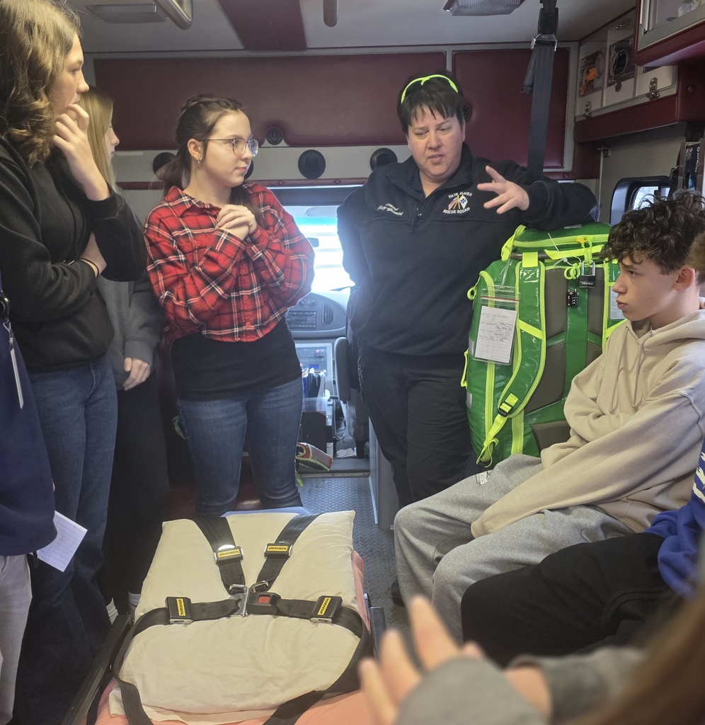 Students stand inside an ambulance listening to a Fair Haven Rescue Squad EMT explain equipment, with a student seated beside a bright green medical pack.